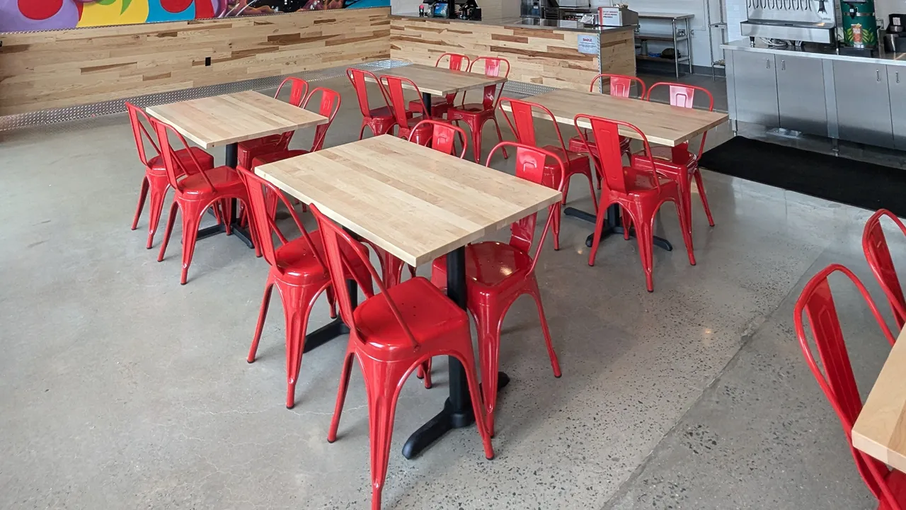 Close-up of interior seating at Dave's Hot Chicken, Passaic Ave, Kearny, NJ, with red chairs and light wood tables.