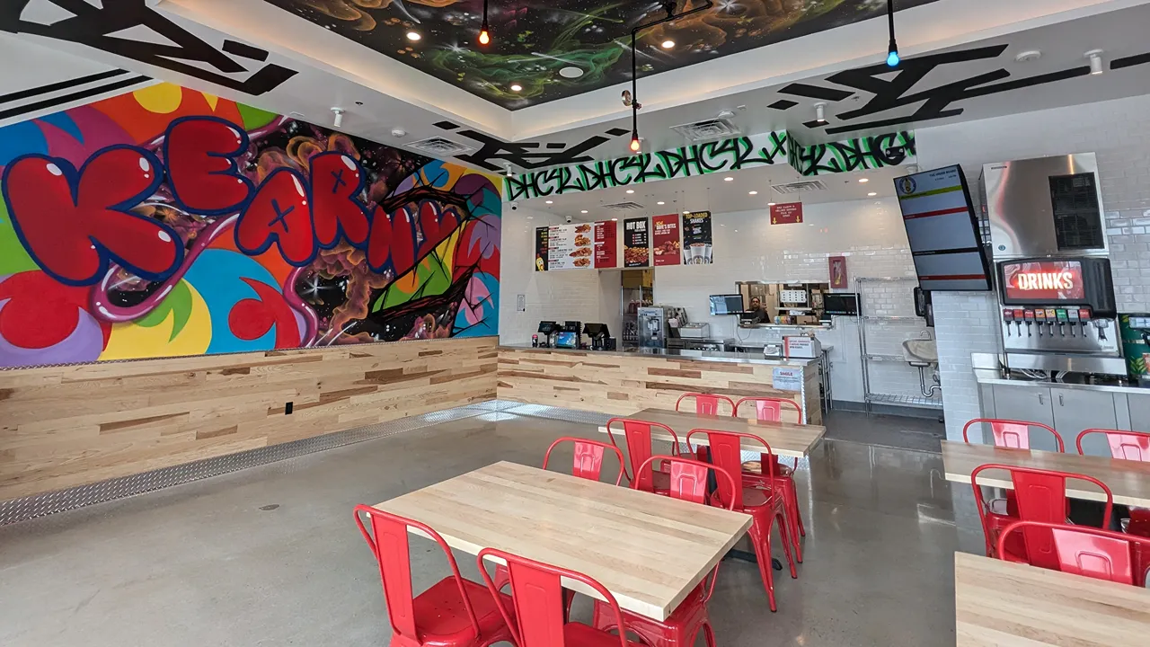 Interior view of Dave's Hot Chicken on Passaic Ave, Kearny, NJ, featuring vibrant wall murals and red seating.