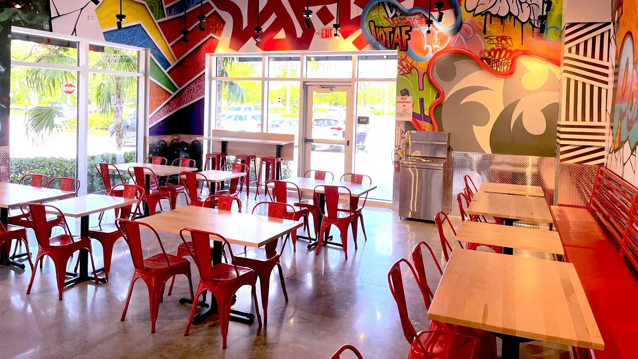 Spacious dining area inside Dave’s Hot Chicken on Pines Blvd, Pembroke Pines, FL - West Fork, featuring red chairs and tables near large windows.