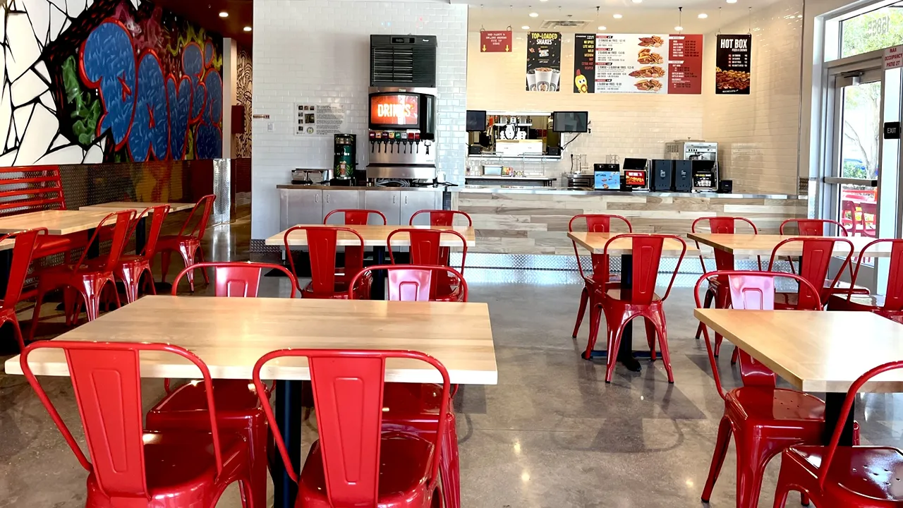 Service counter with tables and chairs in the dining area of Dave’s Hot Chicken on Pines Blvd, Pembroke Pines, FL - West Fork, with vibrant wall murals in the background.