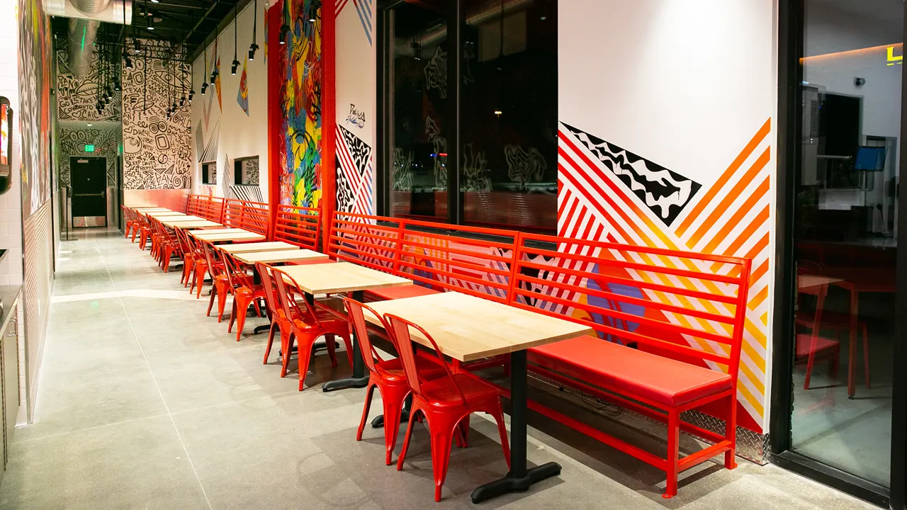 Interior seating at Dave's Hot Chicken on Preston Rd, Plano, TX - Frisco location, with colorful wall art and red chairs.