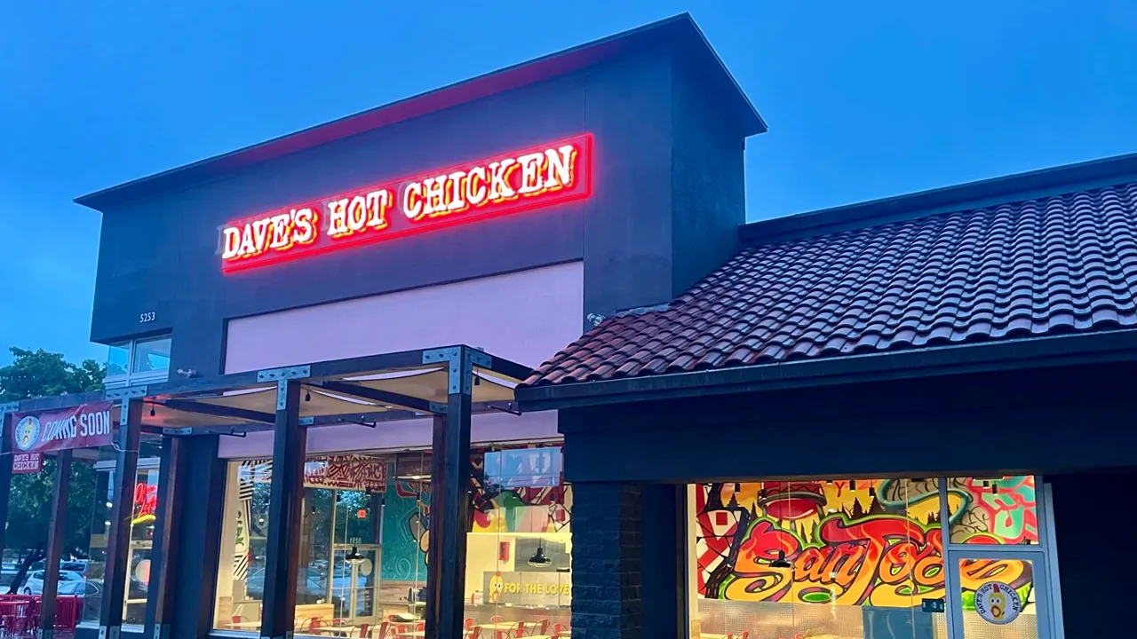 Exterior of Dave's Hot Chicken on Prospect Rd, San Jose, CA, with a neon sign and colorful mural visible through the windows.