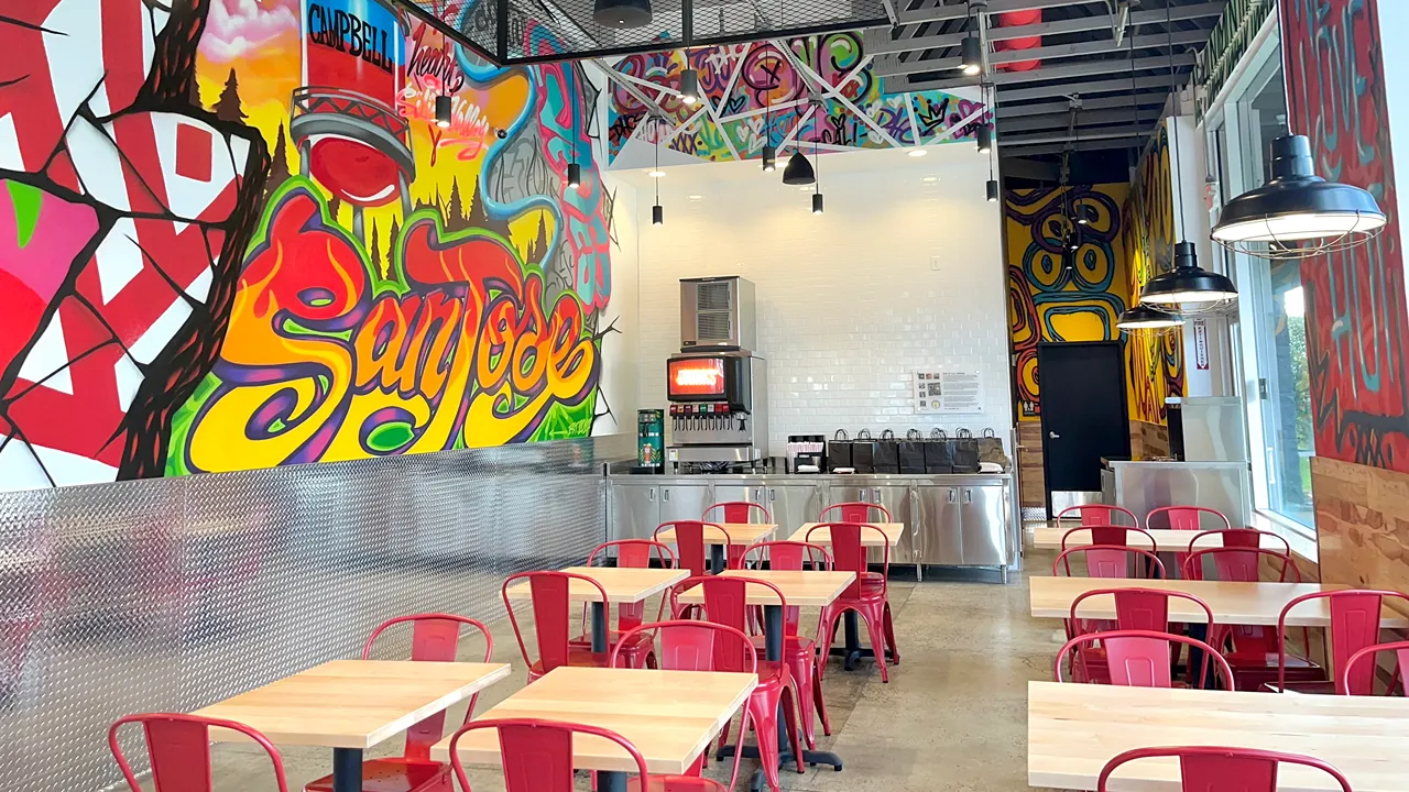 Interior dining area of Dave's Hot Chicken on Prospect Rd, San Jose, CA, featuring colorful murals and red chairs.