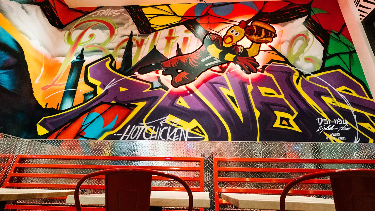 Dining area with red metal chairs and wooden tables, set against colorful mural walls at Dave’s Hot Chicken, located on Reisterstown Rd, Owings Mills, MD.