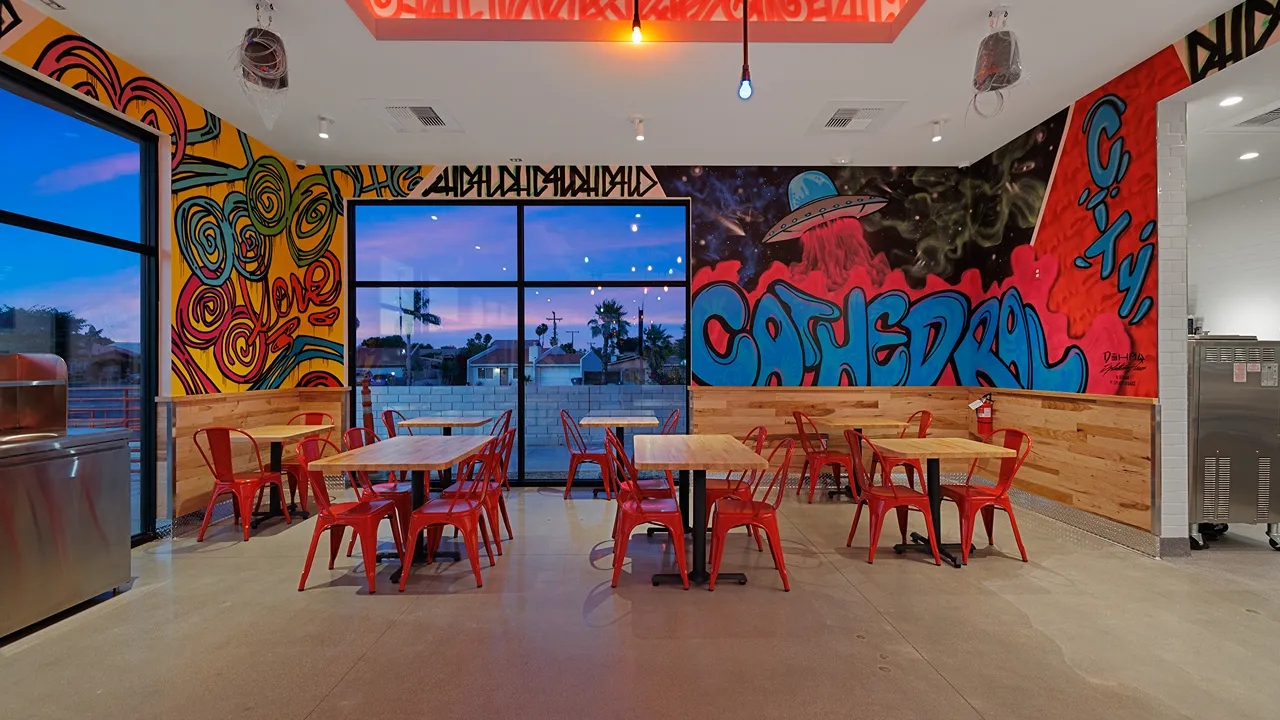 Interior of Dave's Hot Chicken restaurant on Date Palm Drive, Cathedral City, CA, with red chairs and colorful graffiti murals.