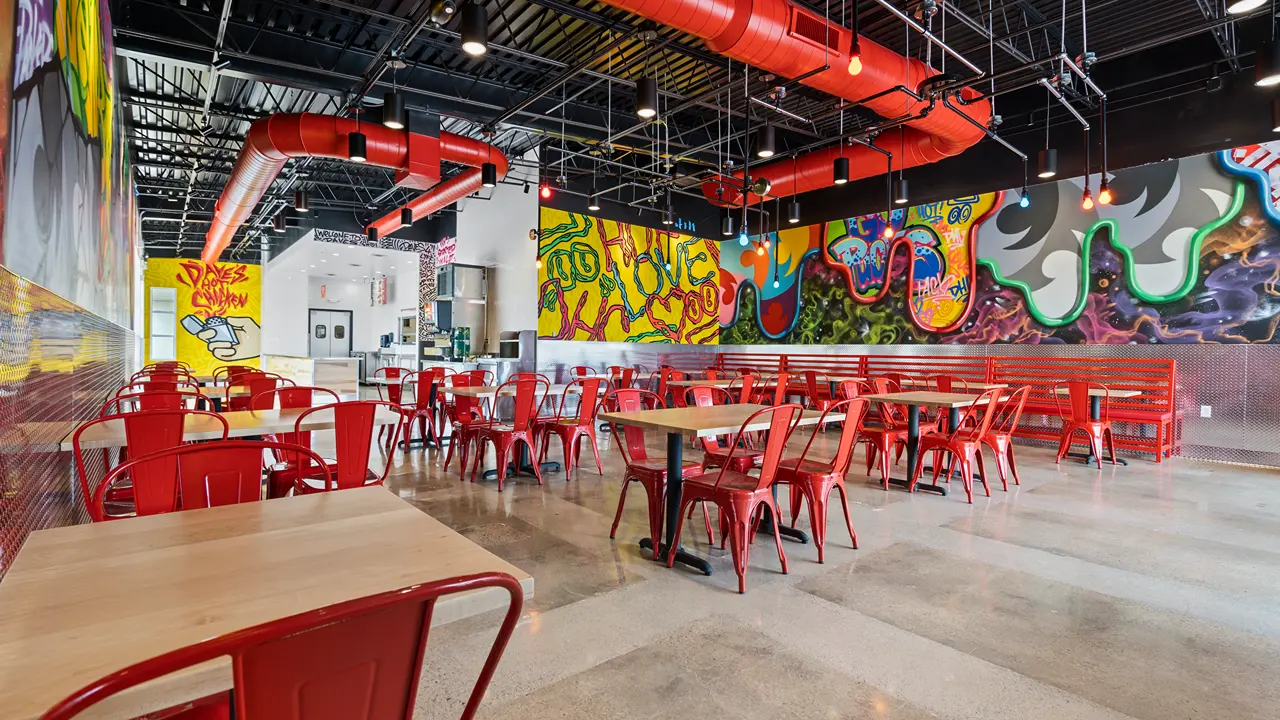 Spacious seating area at Dave's Hot Chicken in Ashwaubenon, WI, near Green Bay, featuring bright red chairs and wall murals.