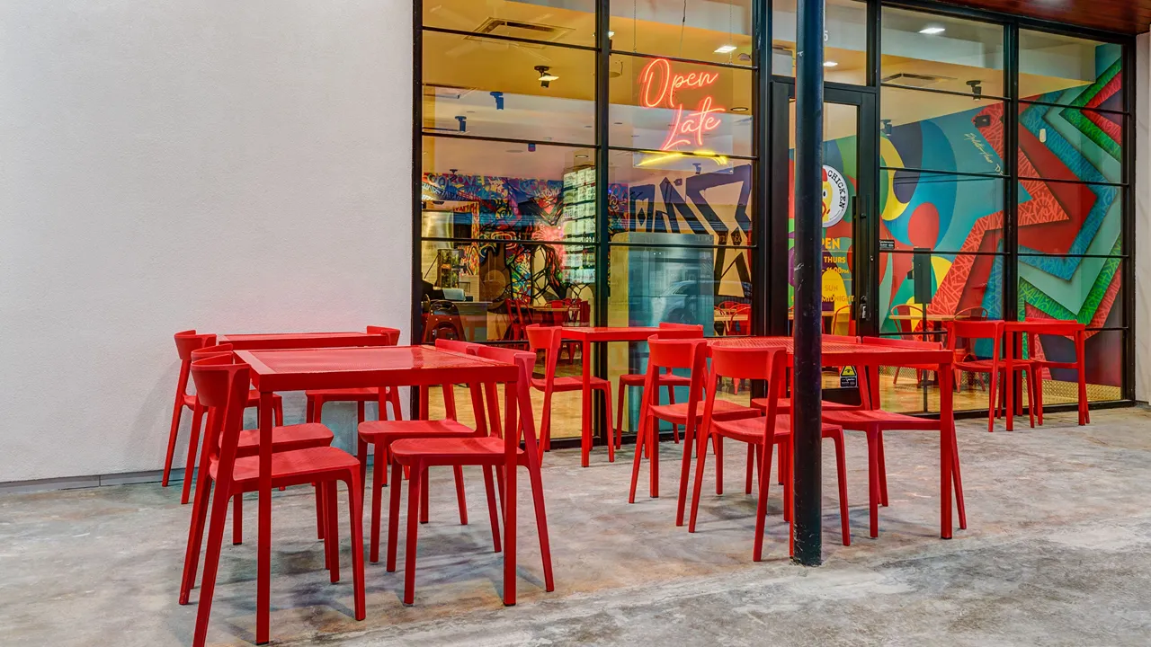 Outdoor patio seating with red tables and chairs at Dave's Hot Chicken on Rice Blvd, Houston, TX.