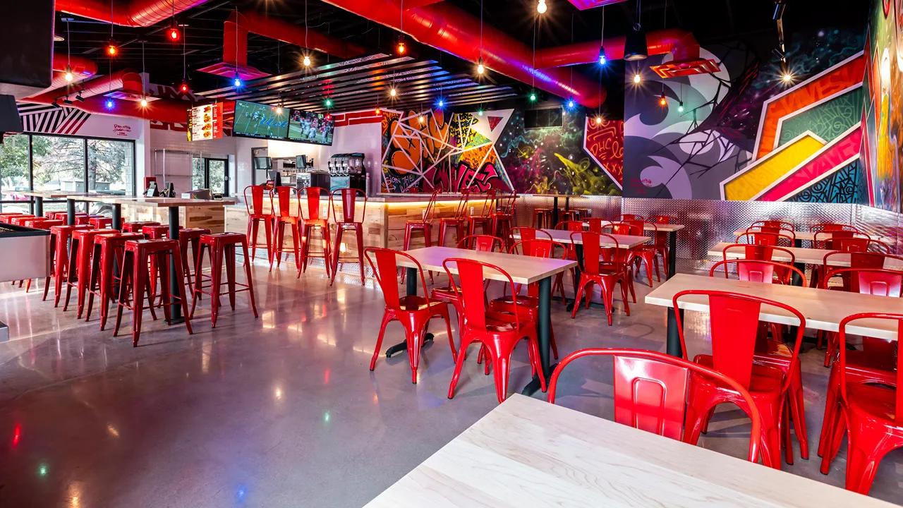 View of the counter area with red bar stools and artistic graffiti-style walls inside Dave’s Hot Chicken in Fort Collins, CO.