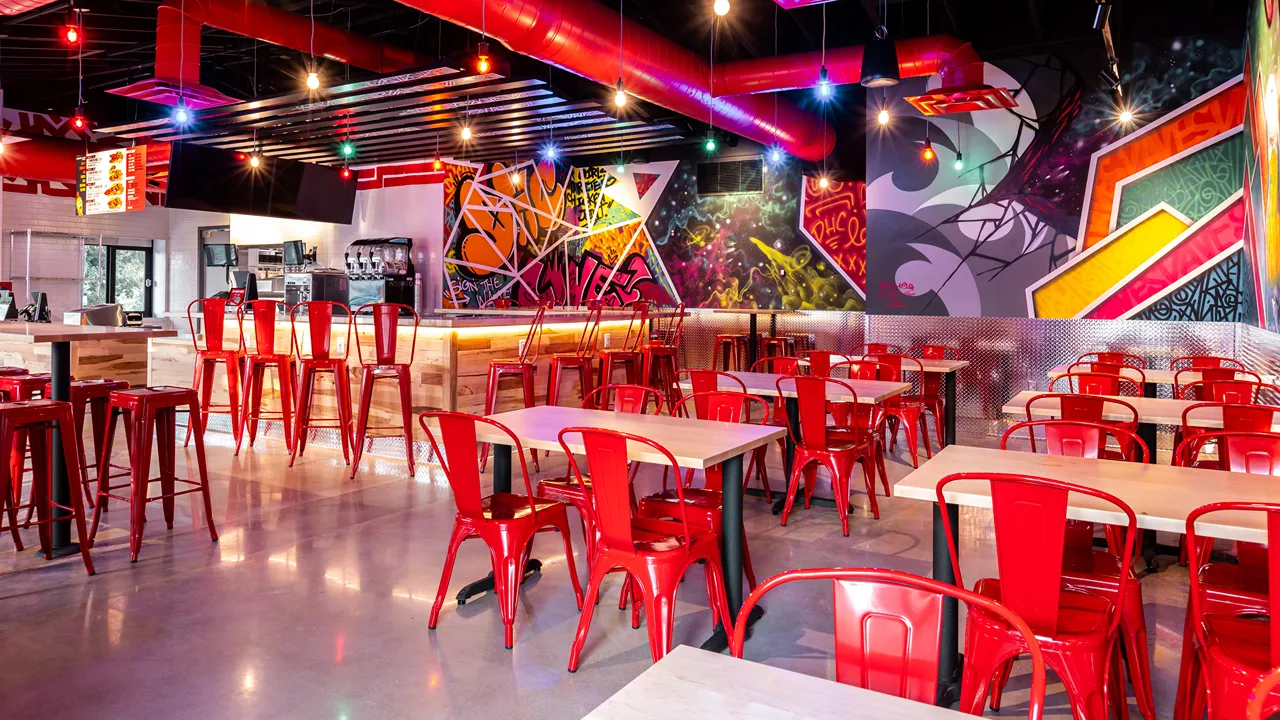 Counter area with red bar stools and graffiti-style walls inside Dave’s Hot Chicken, Fort Collins, CO.