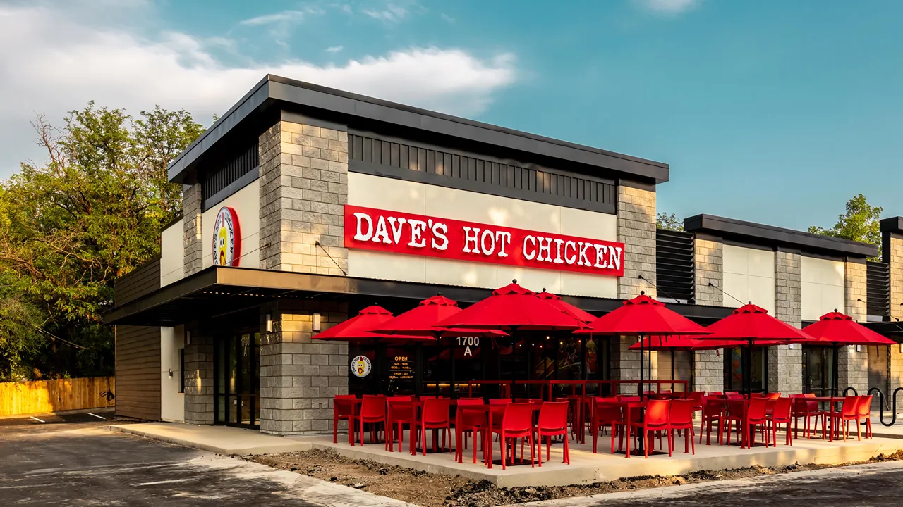 Exterior of Dave’s Hot Chicken with red patio seating, umbrellas, and bright signage at the Fort Collins, CO location on College Ave.