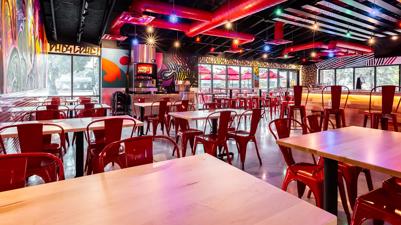 Spacious seating area with red chairs and large windows, illuminated with colorful hanging lights inside Dave’s Hot Chicken in Fort Collins, CO.