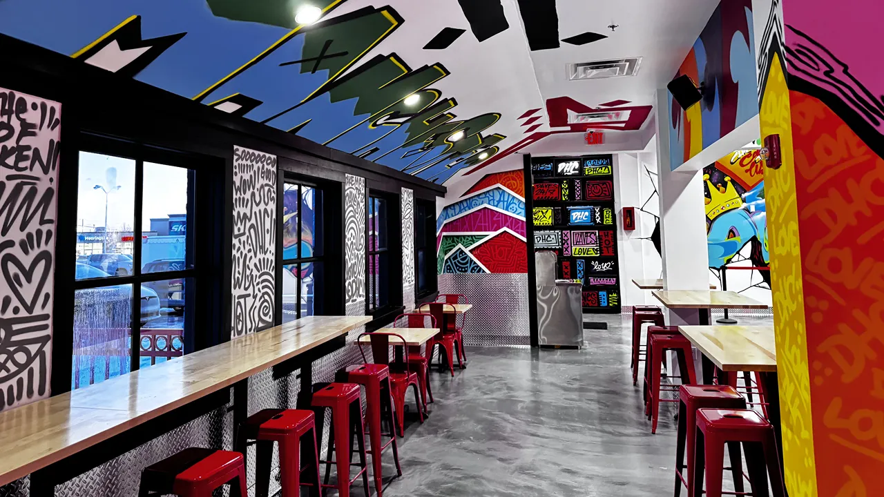 Spacious dining area inside Dave's Hot Chicken on S. Willow St., Manchester, NH, featuring bold murals, red seating, and long tables.