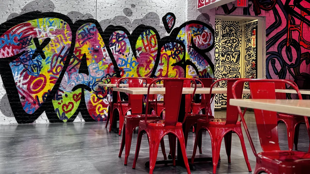 Interior seating area of Dave's Hot Chicken on S. Willow St., Manchester, NH, with red chairs, wooden tables, and bench seating by the windows.