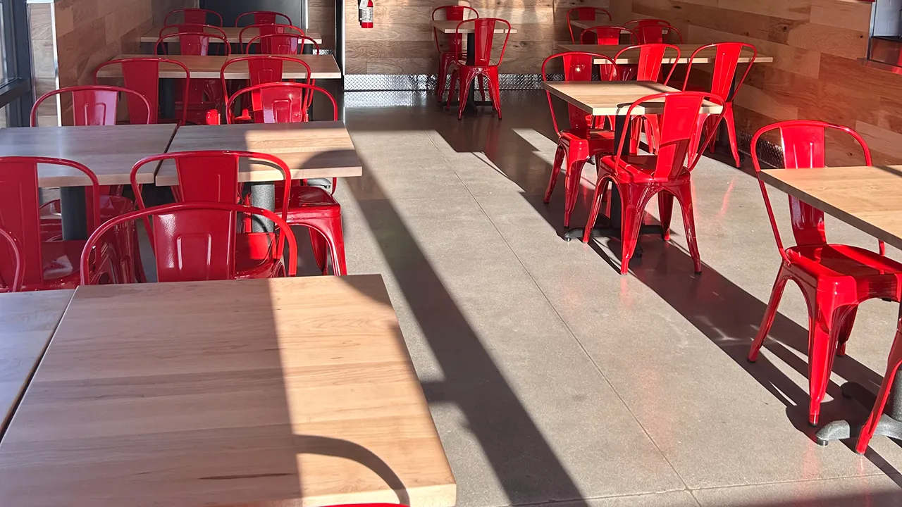 Dining area with red chairs and wooden tables at Dave's Hot Chicken, S. Yuma Palms Pkwy, Yuma, AZ.