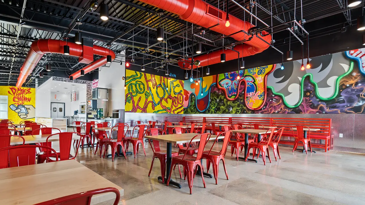 Interior view of Dave's Hot Chicken in Ashwaubenon, WI, near Green Bay, showcasing red seating and artistic murals.