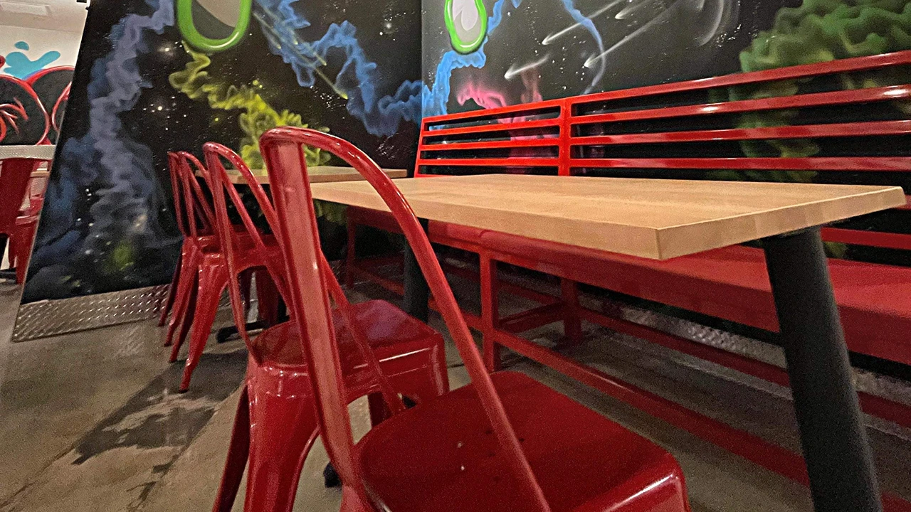 Cozy corner inside Dave's Hot Chicken in Altamonte Springs, FL, with bright red chairs, bench seating, and colorful mural backdrop.