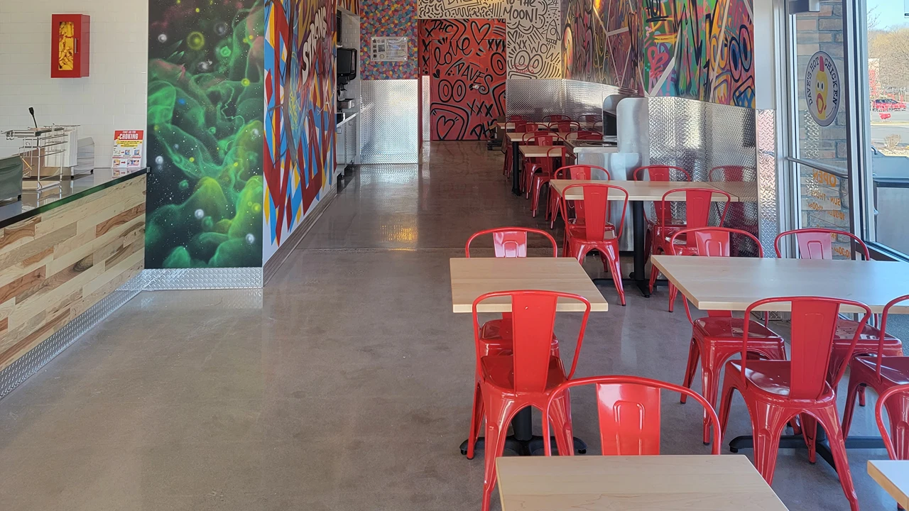 Bright red seating area inside Dave's Hot Chicken in Amsterdam, NY, with colorful murals along the walls.