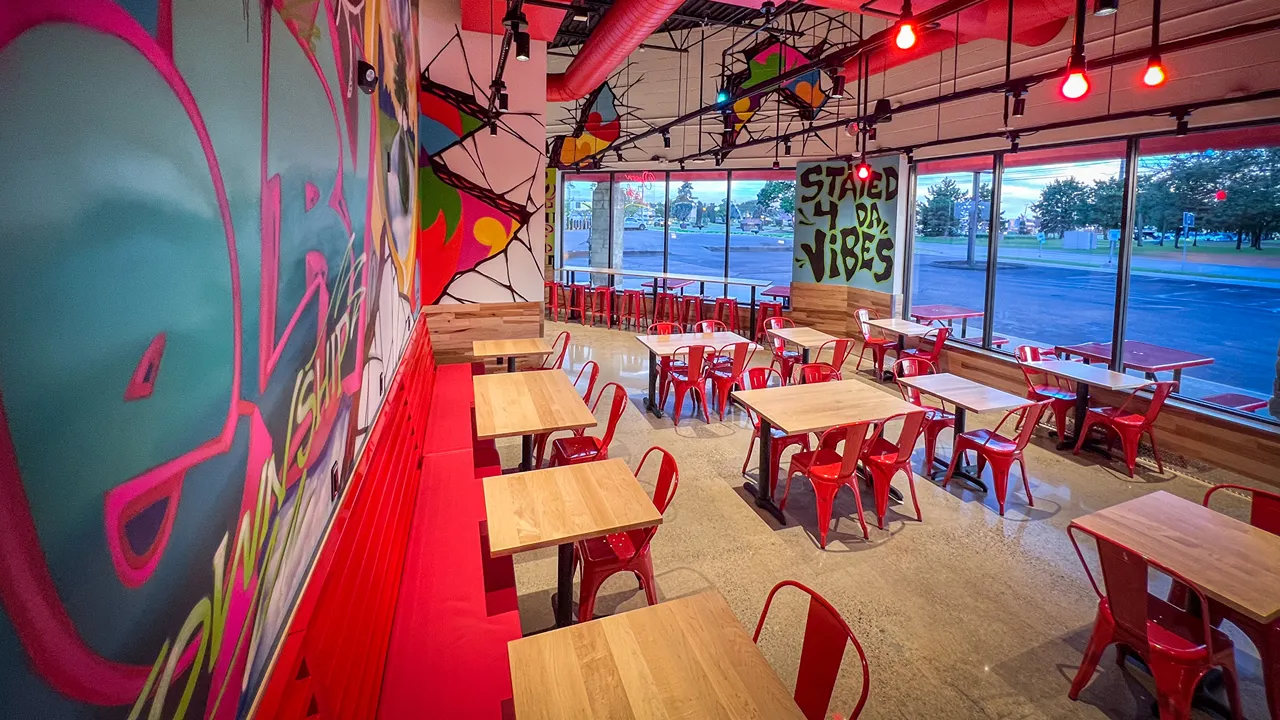 Spacious interior of Dave's Hot Chicken in Shelby Township, MI, with red chairs and large wall art.