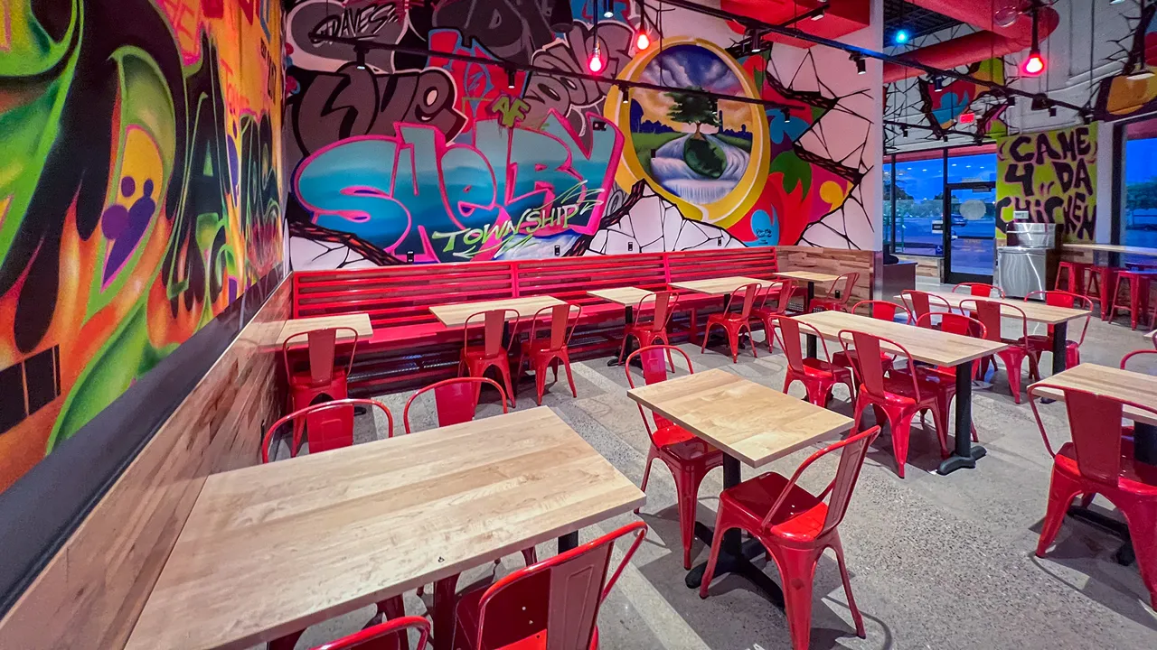 Vibrant indoor dining area at Dave's Hot Chicken in Shelby Township, MI, featuring Shelby Township mural and red seating.