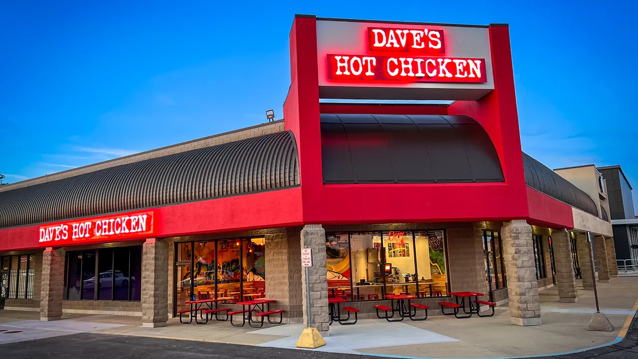 Evening exterior shot of Dave's Hot Chicken, Shelby Township, MI, showing bright red signage and building design.