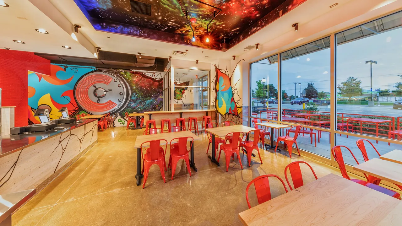 Counter and seating area with a mural of a circular design and vibrant colors at Dave's Hot Chicken on Showplace Dr., Naperville, IL.