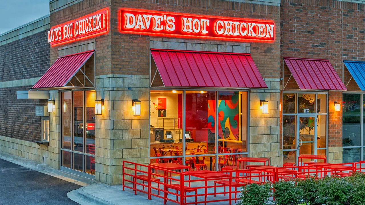 Exterior view of Dave’s Hot Chicken on Showplace Dr., Naperville, IL, featuring bold red signage, canopy-covered windows, and spacious outdoor seating.