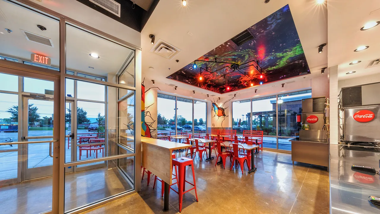 Bright dining area with red chairs, colorful murals, and varied seating options including stools, benches, and standard seats at Dave's Hot Chicken on Showplace Dr., Naperville, IL.