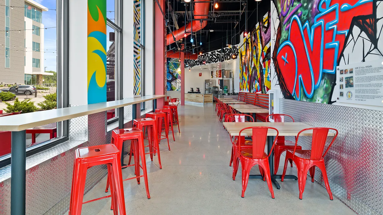 Interior dining area of Dave's Hot Chicken on Sligo Drive, Madison, WI, featuring red seating, wooden tables, and vibrant murals.