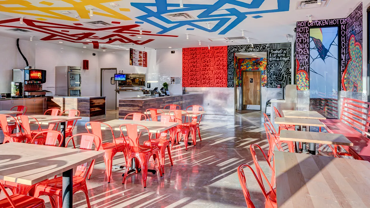 Interior view of the dining area at Dave's Hot Chicken on Kuykendahl Road, Spring, TX, with red chairs and vibrant wall art.