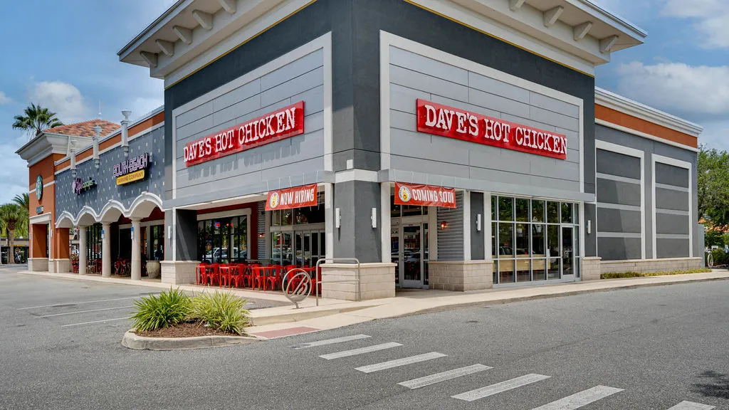 Modern exterior of a Dave’s Hot Chicken restaurant in Gainesville, FL, with large windows and bright red signage