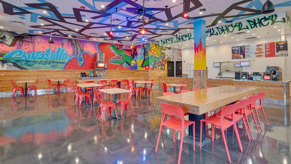 Red chairs and tables with wall murals of a green alligator and bold text inside the dining area of Dave’s Hot Chicken in Gainesville, FL.