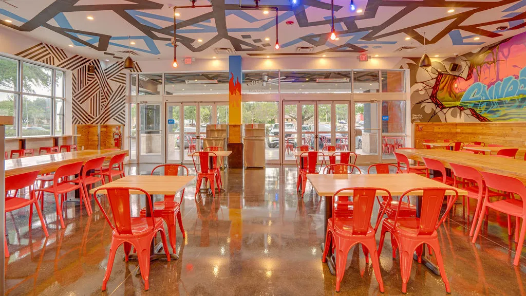 Spacious dining area with modern seating, vibrant murals, and floor-to-ceiling windows inside Dave’s Hot Chicken in Gainesville, FL.