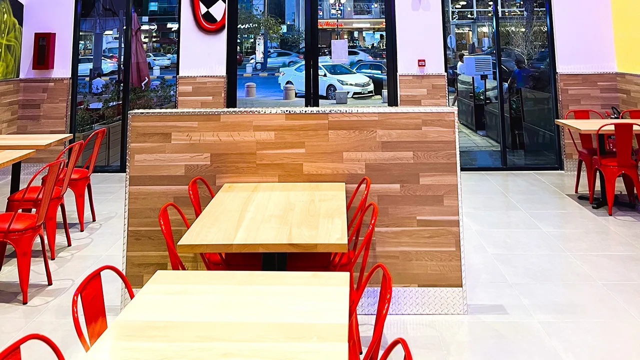 Close-up of seating area inside Dave's Hot Chicken, Riyadh, with red chairs and wooden tables on Tahliah Street, Al Olaya.