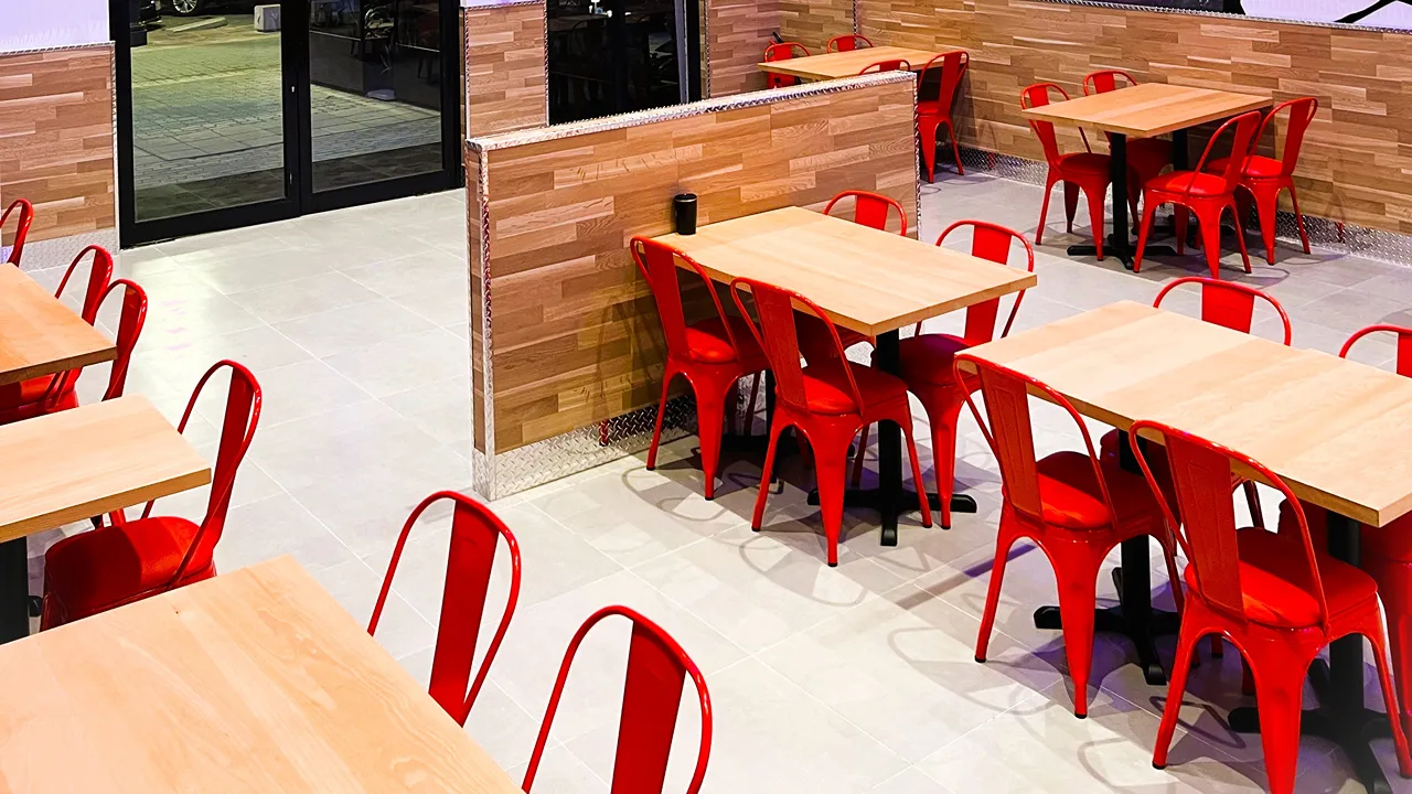 Seating area with wooden tables and red chairs inside Dave's Hot Chicken, Riyadh, on Tahliah Street, Al Olaya
