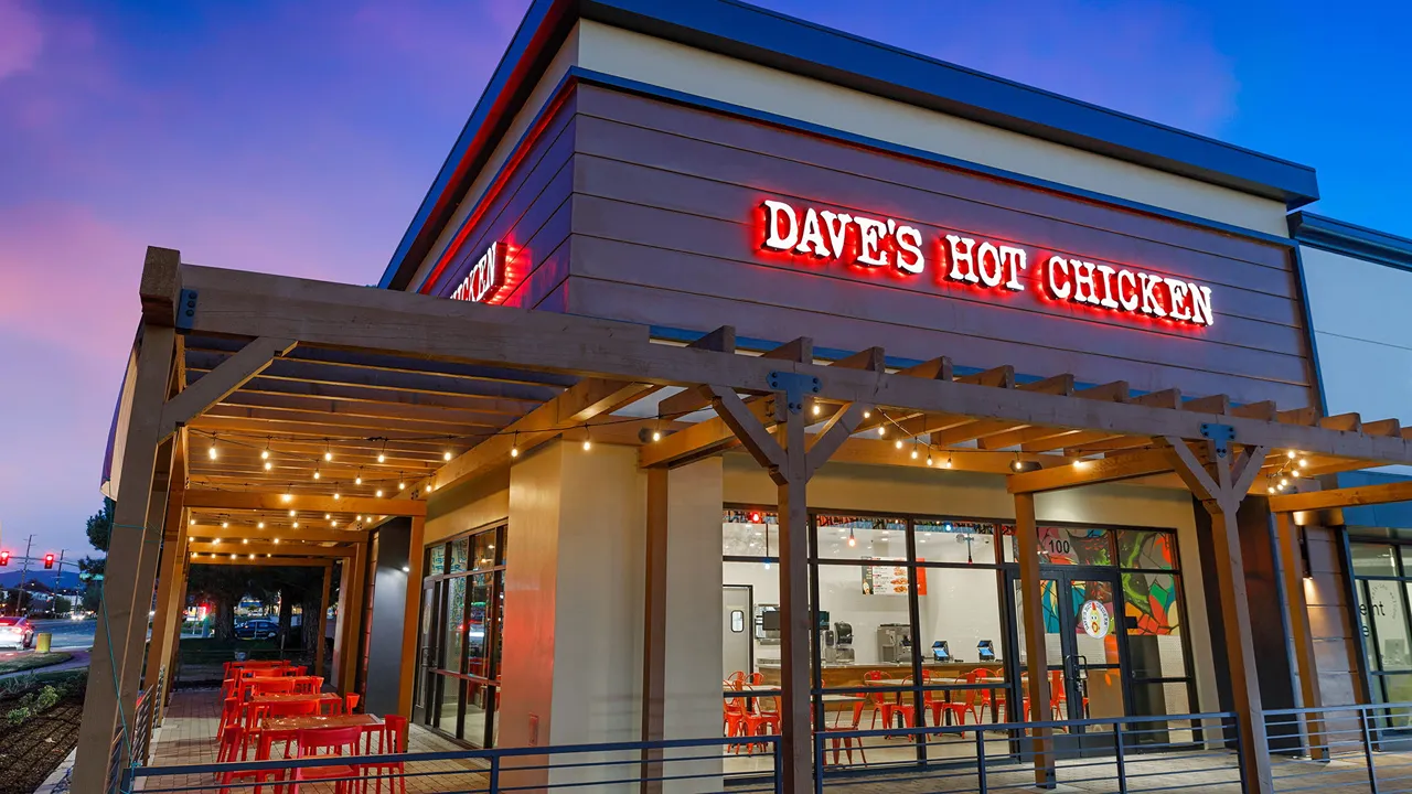 Exterior view of Dave's Hot Chicken on Temecula Pkwy in Temecula, CA, with string lights and red outdoor seating.