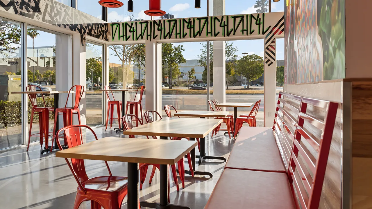 Spacious seating area inside Dave's Hot Chicken on Hawthorne Blvd, Torrance, CA, with red chairs, wooden tables, and large windows.