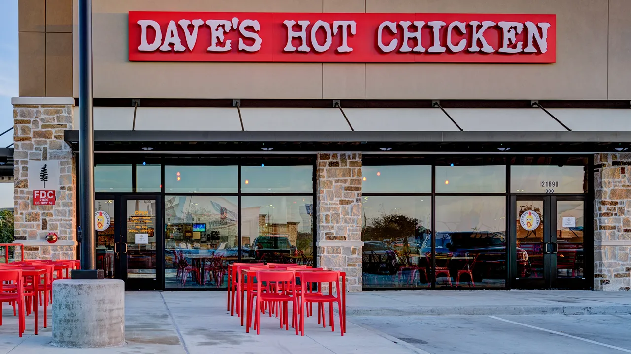 Exterior view of Dave’s Hot Chicken with red signage and outdoor seating, US Hwy 59, Valley Ranch, New Caney, TX.