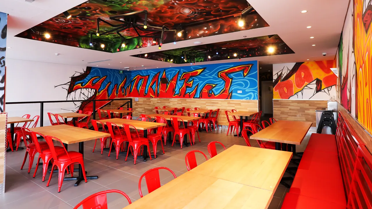 Brightly lit dining area inside Dave's Hot Chicken on Uthman Ibn Affan Branch Rd, Riyadh, KSA, featuring colorful decor.