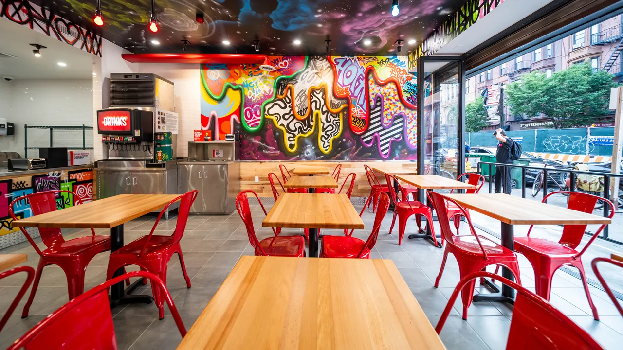 A vibrant seating area inside Dave's Hot Chicken in Brooklyn, NY, featuring colorful graffiti art and red chairs.