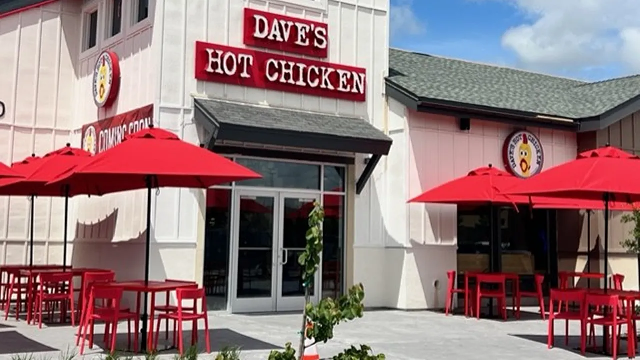 Outdoor seating with red umbrellas at the front of Dave’s Hot Chicken on Vintage Way, Novato, CA.