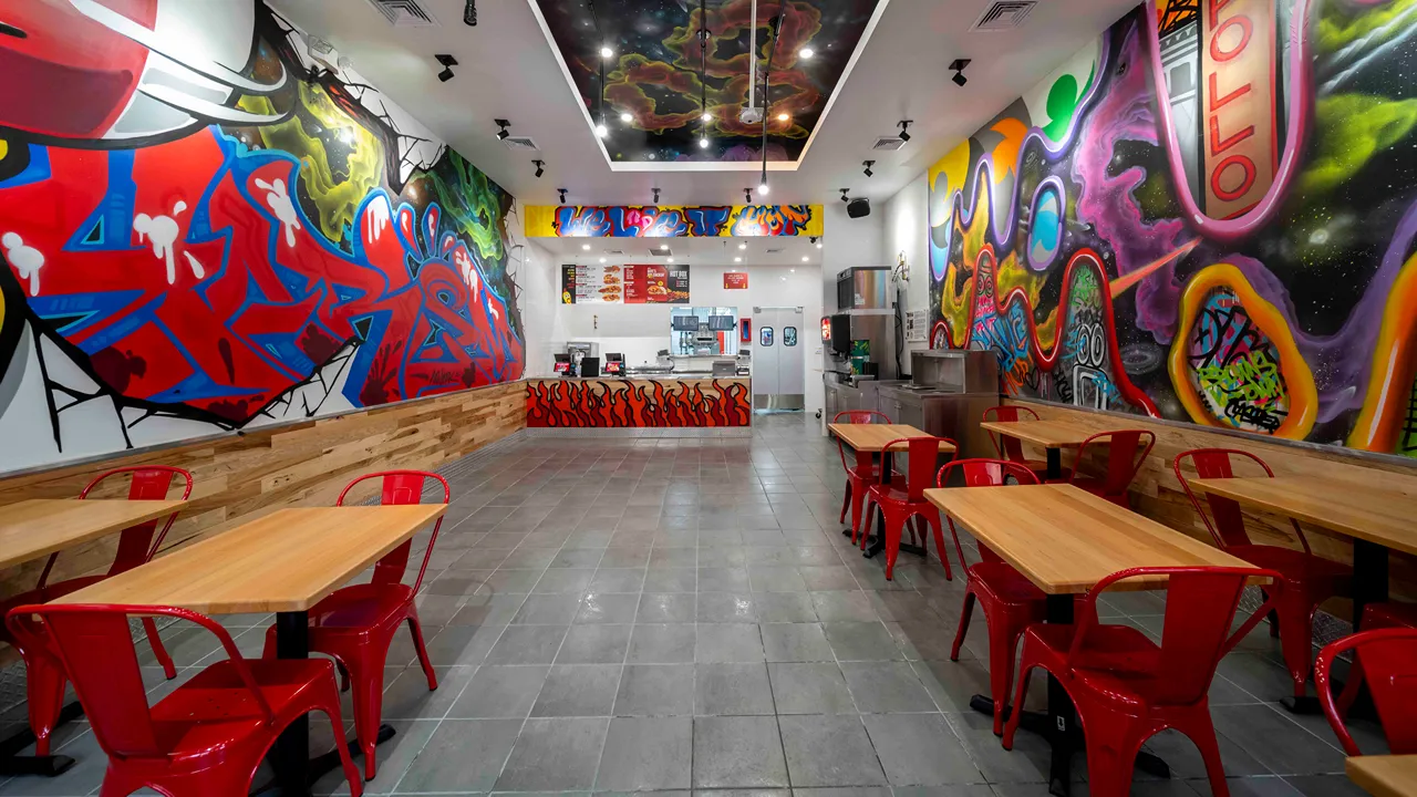 Bright dining and service area with red chairs, vibrant murals, and a colorful ceiling at Dave’s Hot Chicken, W. 125th St., Harlem, New York, NY.