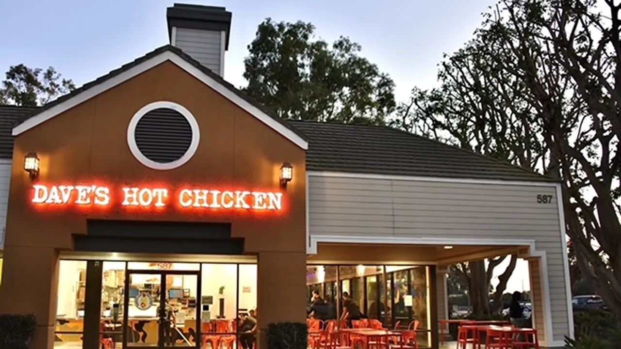 Exterior of Dave’s Hot Chicken on W. Channel Islands Blvd, Port Hueneme, CA, featuring outdoor seating with red umbrellas and storefront signage.