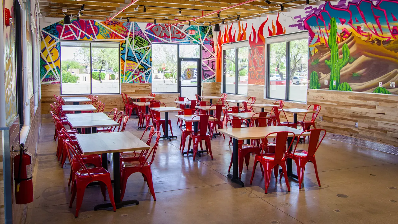 Interior seating area of Dave's Hot Chicken on W. Costco Dr, Marana, AZ, with red chairs and wooden tables in a colorful space.