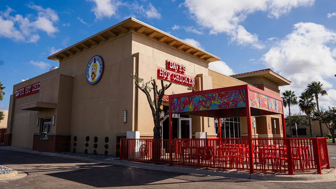 Exterior angled view of Dave's Hot Chicken on W. Expressway 83, McAllen, TX, featuring the drive-through window, bright signage and a colorful mural over the entrance.