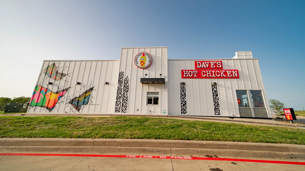 Exterior front view of Dave's Hot Chicken in Waco, TX on Jack Kultgen Fwy, featuring signage and vibrant murals.