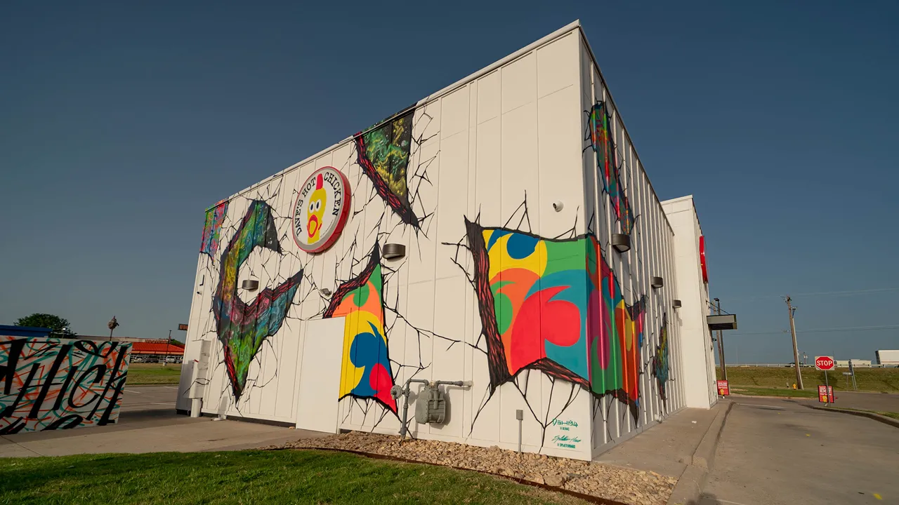 Side exterior view of Dave's Hot Chicken in Waco, TX on Jack Kultgen Fwy, showing the mural-covered side wall of the building.