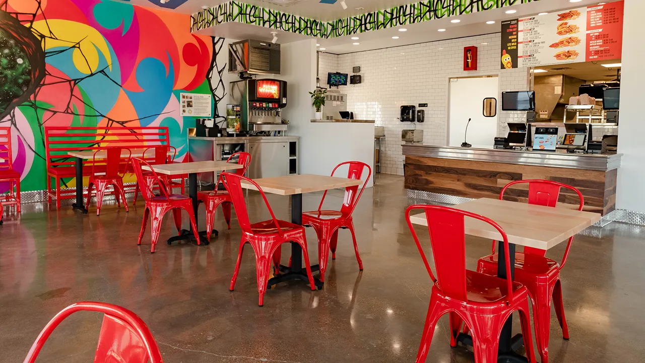 Interior of Dave's Hot Chicken in Waco, TX on Jack Kultgen Fwy, showing red chairs and tables with colorful wall art.