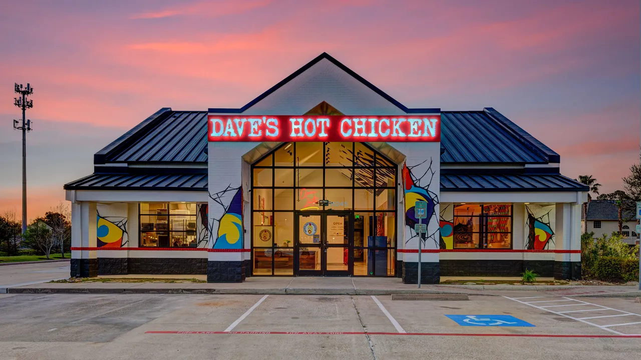 Front view of Dave's Hot Chicken with colorful murals, bright neon signage and a modern glass entry at Wallisville Rd, Houston, TX.