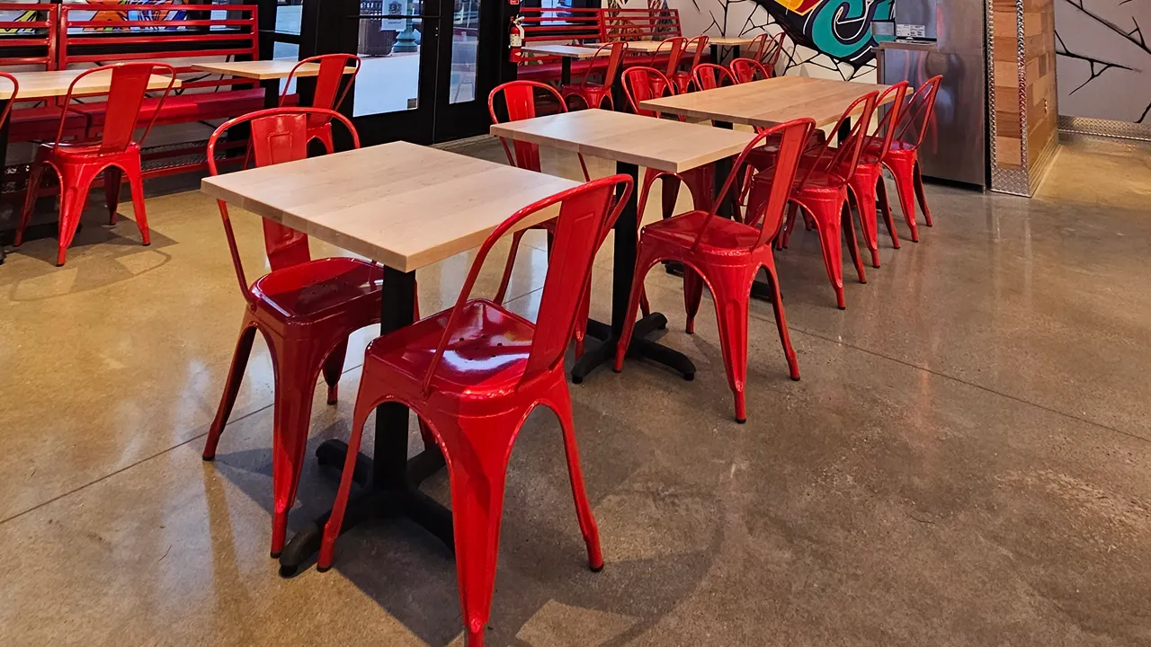 Close-up of seating at Dave's Hot Chicken, Westley on Broadway, Kansas City, MO, with red chairs and wooden tables.