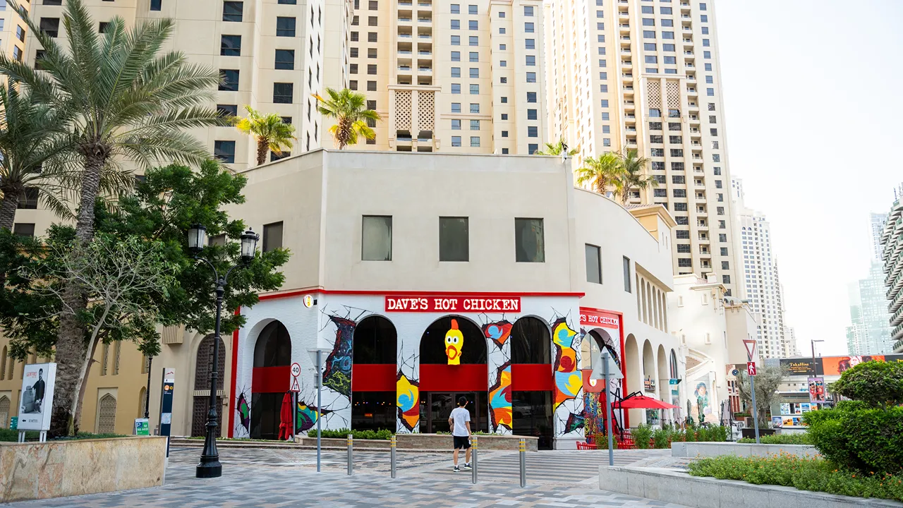 Exterior view of Dave's Hot Chicken with murals, surrounded by high-rise buildings at The Walk, Jumeirah Beach Residence, Dubai, UAE.